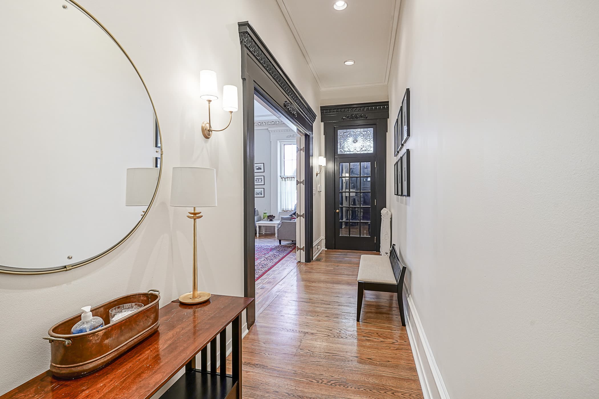 Entry hall with round brass mirror, console table and glass-paneled door crowned by a stained-glass transom