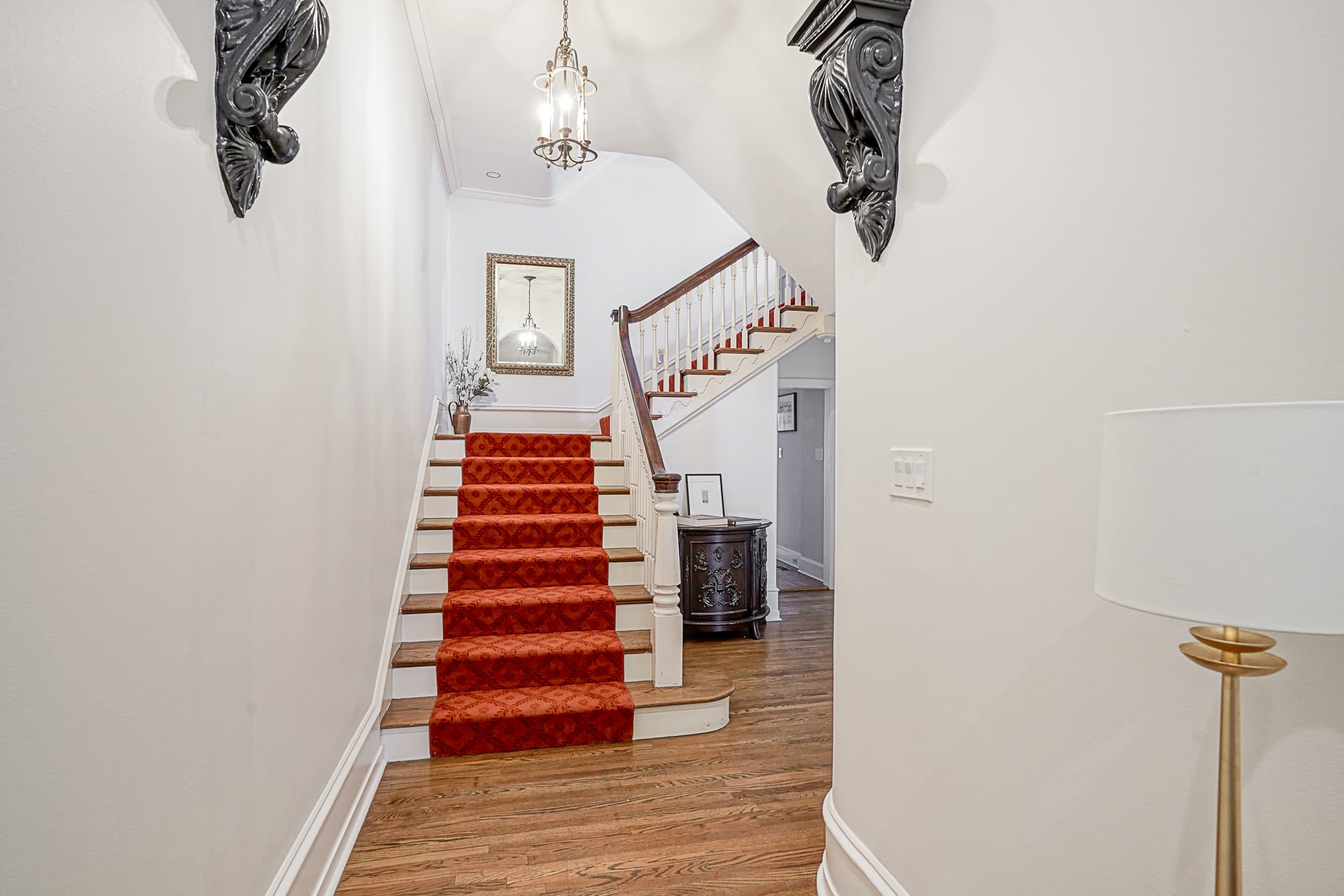 Main staircase with red patterned runner and brass lantern pendant, framed by carved black corbels