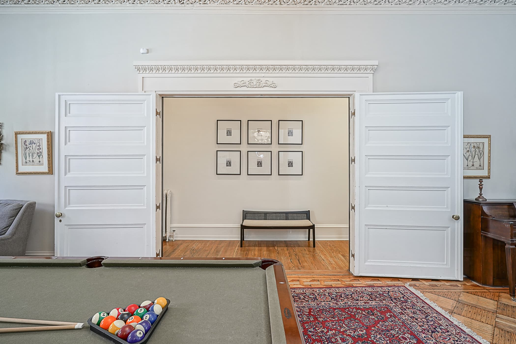 Grand parlor with pool table opening through towering pocket doors beneath carved plaster friezes
