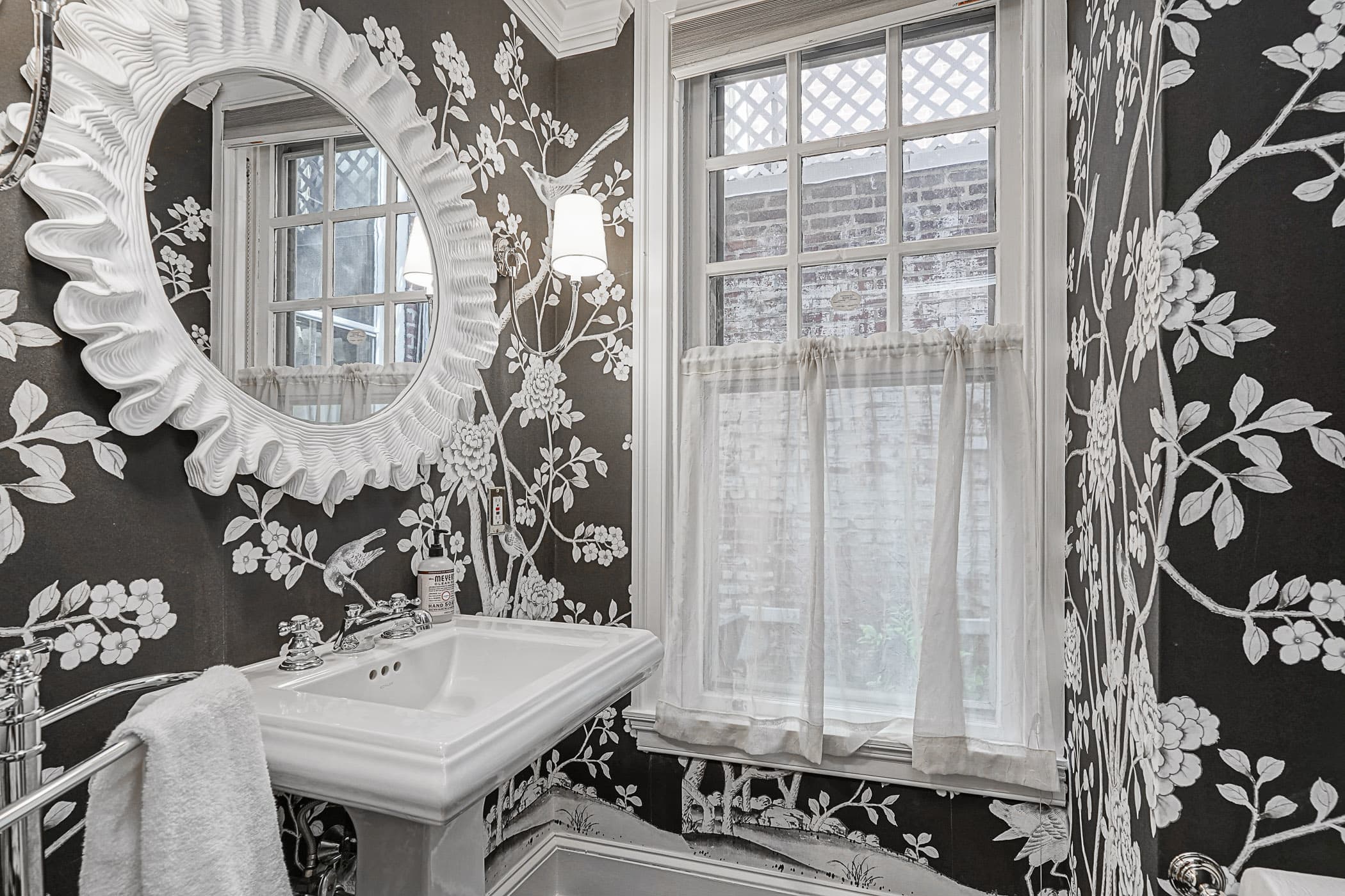Powder room wrapped in black-and-white chinoiserie wallpaper with a sculpted white mirror